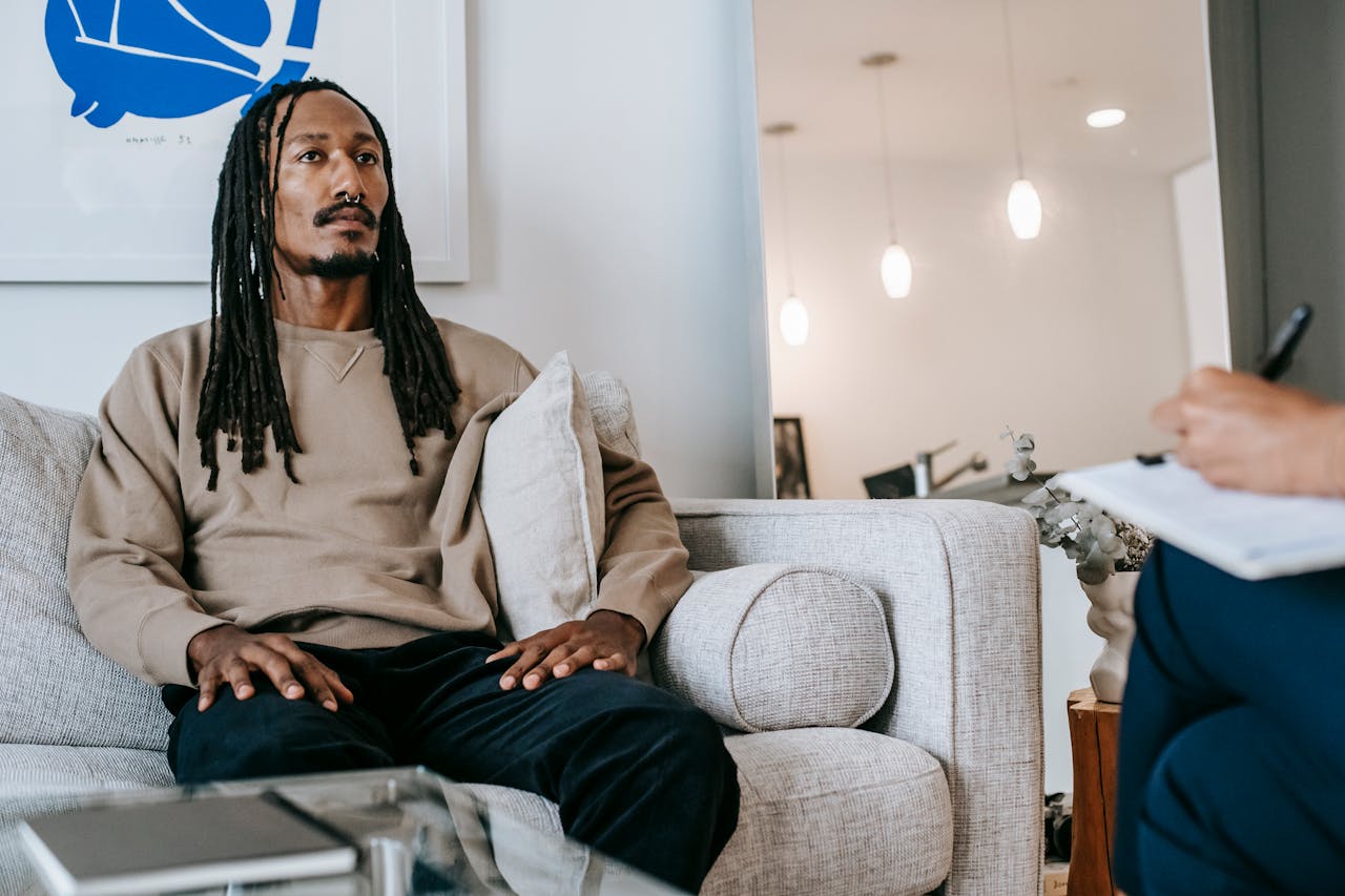 Mastering the First Impression: Your intriguing post title goes here Pensive African American male client with dreadlocks sitting on couch with hands on laps near crop psychologist with clipboard during appointment